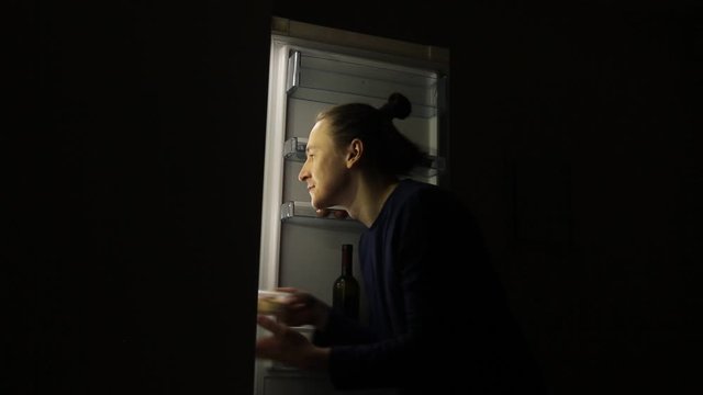 Hungry Man with eating disorder Looking in a Fridge Taking Food at Night. Concept of unhealthy lifestyle