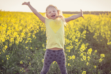Naklejka na ściany i meble adorable charming blond girl with hands up jumping in yellow meadow