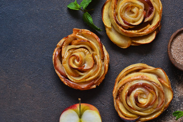 Dish of apple roses baked in puff pastry on a dark concrete background with apples. View from above