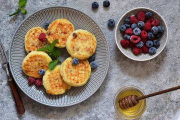 Cheesecakes with berries and honey for breakfast on a gray concrete background. View from above.