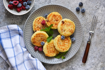 Cheesecakes with berries and honey for breakfast on a gray concrete background. View from above.