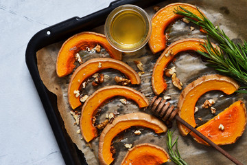 Baked sweet pumpkin with honey and rosemary on a tray on a gray concrete background. View from...
