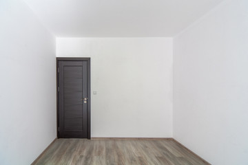 Closed wooden door in empty room, wooden flooring. White walls