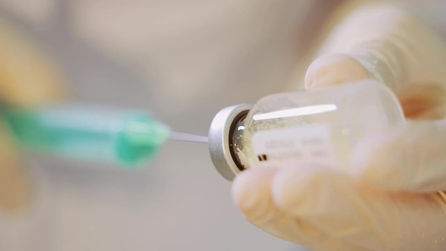 A white-gloved healthcare worker is preparing an injection with a syringe, hypodermic needle and vial. Flu vaccine.