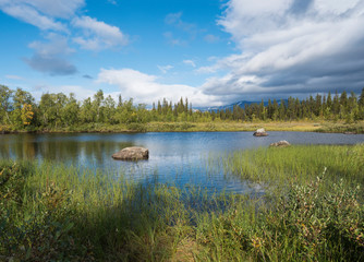 Beautiful northern landscape with river basin of Kamajokk, boulders, mountain peaks and spruce tree forest in Kvikkjokk in Swedish Lapland. Summer sunny day, dramatic clouds