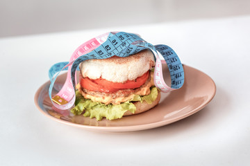 Healthy Lifestyle. Hamburger and tape measure isolated on kitchen table close-up