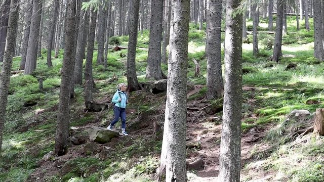 Girl traveler with a backpack goes through the green forest.