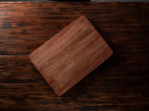Tabla de cortar sobe fondo de madera, vista cenital. Cutting board on a wooden background, overhead view.