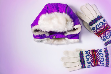 Winter flatlay, warm purple violet hat with earflaps and woolen knitted gloves on a white background. Top view, mockup.