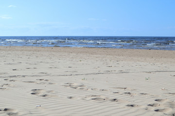 Wavy sand with footsteps on baltic sea coast with wave and blue sky 
