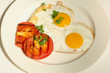 morning food fried eggs from two eggs and slices of grilled tomato on a white plate, white background