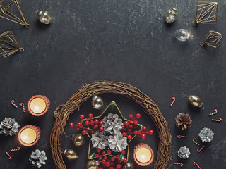 Christmas or New Year composition. Silver-plated fir cones and red berries are in a star bowl. Nearby is a wreath, Christmas decorations and glowing candles. Flat lay / Copy space.