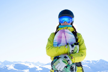 Photo of sportswoman in helmet and goggles with snowboard at ski resort.
