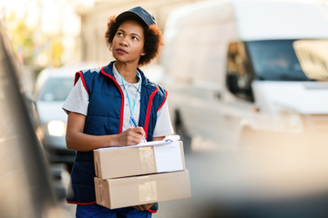 Black female courier writing address while making delivery in the city.