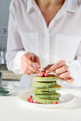 Spirulina pancakes with cranberries on a white table. Woman decorates pancakes with berries.