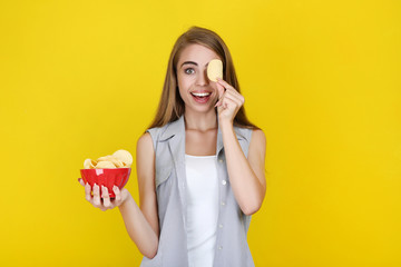 Young beautiful girl with potato chips in bowl on yellow background