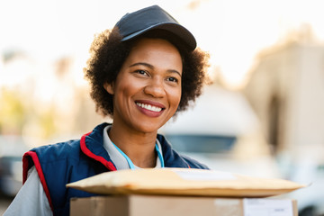 Happy African American female courier with packages in the city.