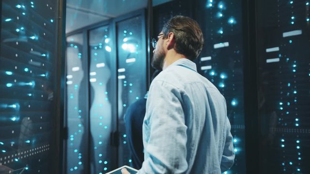 IT administrator checking system quality of server cabinets working on rack. Team of server technicians collaborating in digital room of data center.