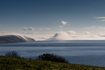 Clouds forming from mist flowing over the cliffs in Whitsand bay Cornwall