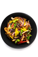 Sliced grilled vegetables, noodles in sauce, sesame seeds in a black plate isolated on white background, top view