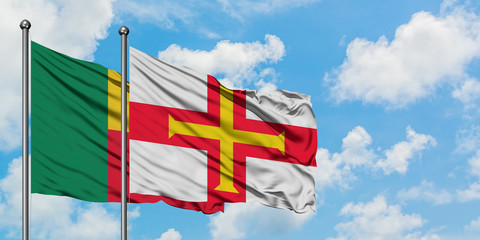 Benin and Guernsey flag waving in the wind against white cloudy blue sky together. Diplomacy concept, international relations.