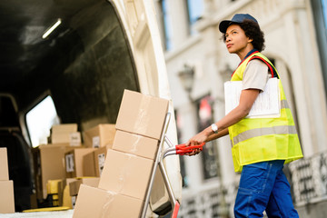 Black female deliverer pushing hands truck while preparing packages for the shipment.