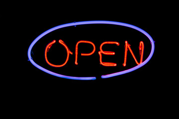 Neon sign open on a black wall.