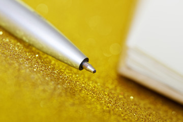 A silver fountain pen lies on a golden background next to a notebook. Time for study and business....