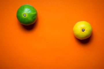 Dos mandarinas, amarilla y verde, sobre fondo naranja