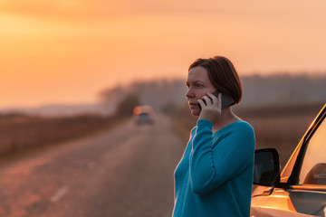 Woman talking on mobile phone by the stopped car