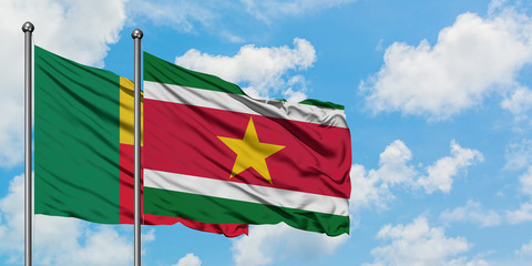 Benin and Suriname flag waving in the wind against white cloudy blue sky together. Diplomacy...