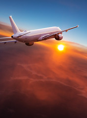 Commercial airplane flying above dramatic clouds during sunset.