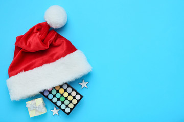 Red santa hat with makeup palette and gift box on blue background