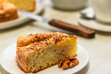 A piece of cake with apples, chopped walnuts and cinnamon lies on a white plate next to a brown knife, close-up