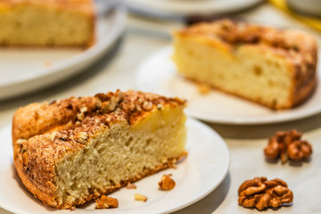 Two pieces of pie with apples, chopped walnuts and cinnamon lie on white plates on a light background