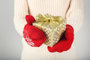 Hands in knitted mittens holding gift box on grey background