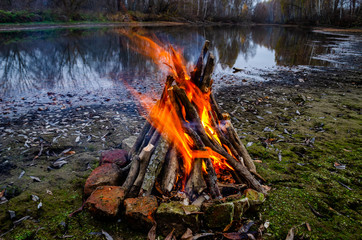 Burning fire on the river Bank. Gloomy autumn day. Hiking and picnic leisure activities.