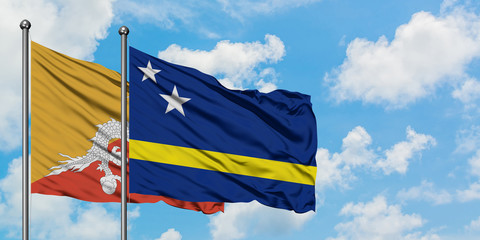 Bhutan and Curacao flag waving in the wind against white cloudy blue sky together. Diplomacy concept, international relations.