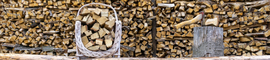 Basket with firewood on wooden background. In a natural light..A basket loaded with chopped wood stands in front of a wall of firewood.