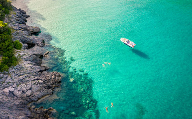 Aerial view of Trsteno beach in Montenegro, near Budva, a boat in a beautiful bay with a rocky shore, blue water, people bathe in clear water