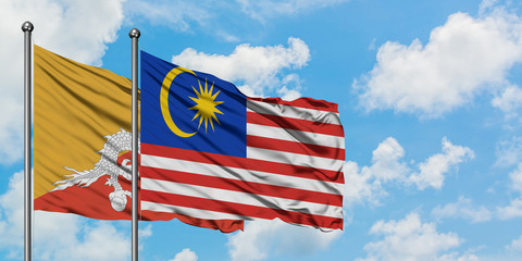 Bhutan and Malaysia flag waving in the wind against white cloudy blue sky together. Diplomacy concept, international relations.