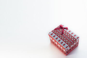A red Christmas box with gifts and a bow stands on a white background with a place for postcard text at an angle to the right. On the box are Christmas trees and snowflakes.