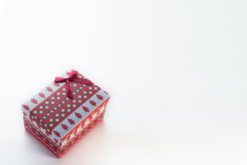 A red Christmas box with gifts and a bow stands on a white background with a place for postcard text at an angle to the left. On the box are Christmas trees and snowflakes.