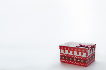 A red Christmas box with gifts and a bow stands on a white background with place for postcard text on the right. On the box are Christmas trees and snowflakes.