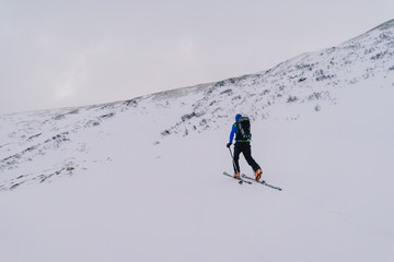 Fototapeta na wymiar Ski alpinist ascending a snow slope in the alps. Winter alpine mountain landscape and ski touring adventure activity. Ski alpinism in the Alpine mountain area, Europe.