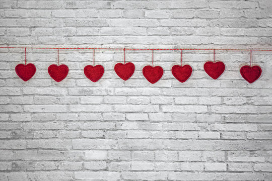 Red handmade textured hearts hanging on a rope on a white brick wall background. Image of Valentines day, birthday, love consept.