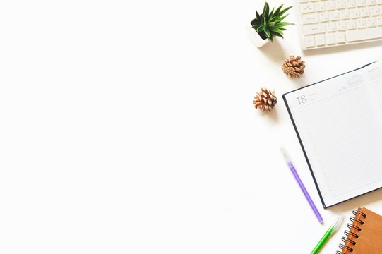White computer keyboard, open paper notebook, purple and green pens, pine cones and decorative plant. Mockup, free space for text. Flat lay photo modern office table with stationery