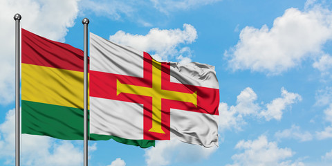 Bolivia and Guernsey flag waving in the wind against white cloudy blue sky together. Diplomacy concept, international relations.