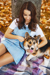 happy woman sits together with Welsh Corgi Pembroke dog in a park outdoors. Young female owner huging pet in park at fall on the orange foliage background. Concept friendship with dog and human