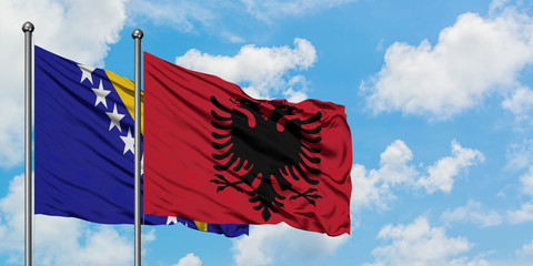 Bosnia Herzegovina and Albania flag waving in the wind against white cloudy blue sky together....